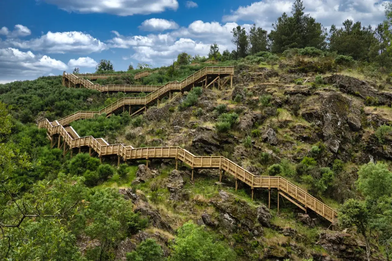 Escaleras de madera serpentean por una ladera verde, invitando al senderismo en Portugal.