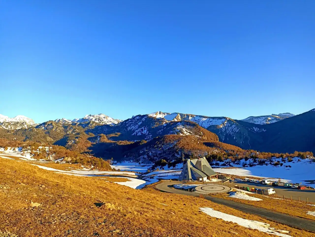 Paisaje invernal en el valle de Belagua con montañas nevadas, un edificio moderno y un aparcamiento.