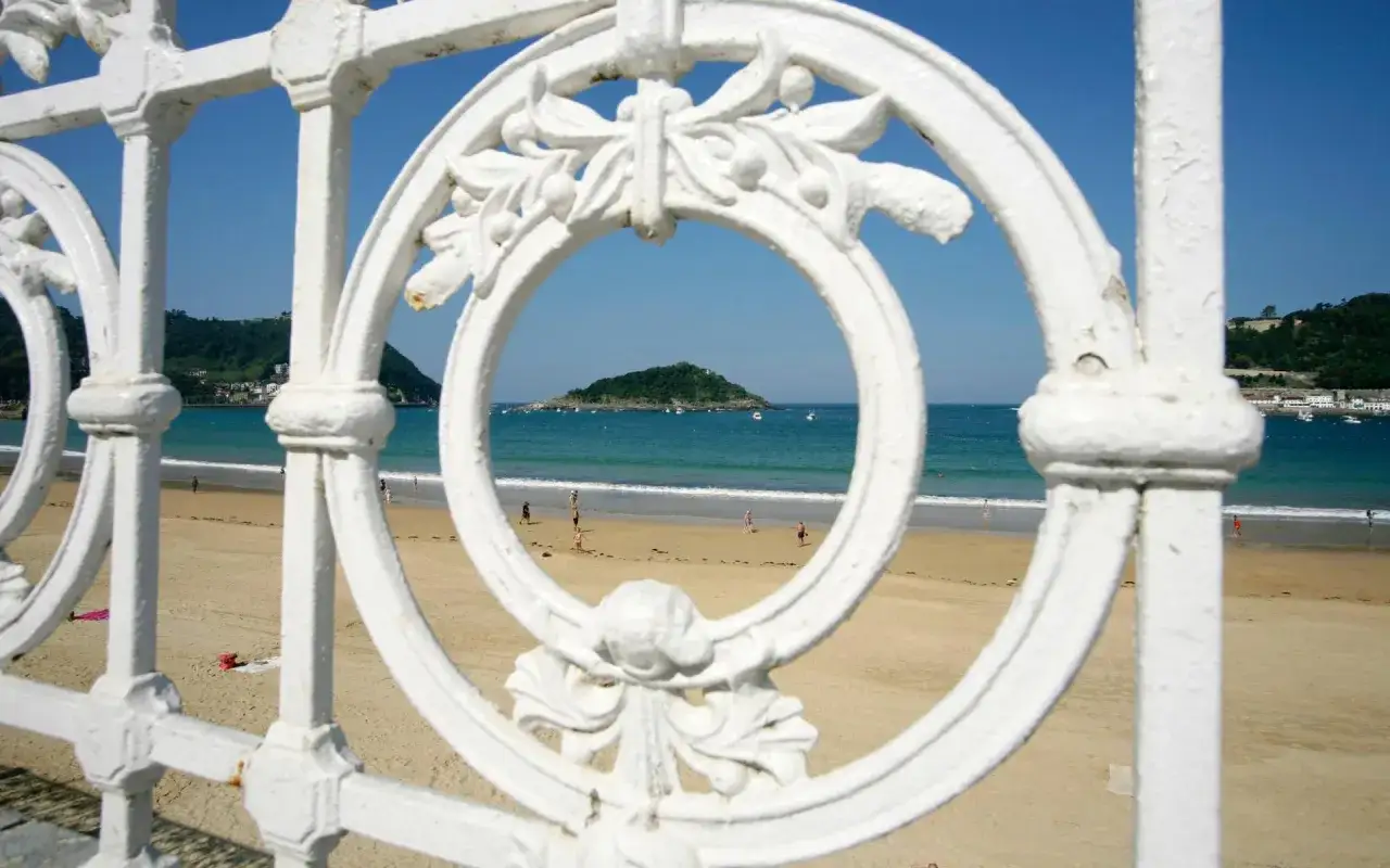 Vista de la playa de la Concha, San Sebastián, a través de una barandilla blanca. Se ve la isla de Santa Clara al fondo, un paraíso que muchos consideran la mejor playa de España.