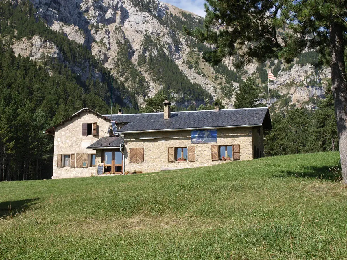 Refugio de montaña en la altitud Pedraforca, rodeado de bosques y con imponentes picos rocosos al fondo.