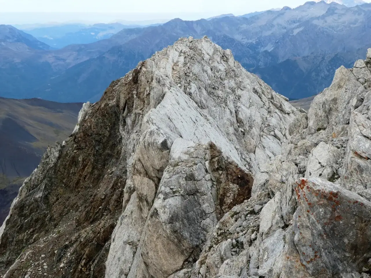 Cima rocosa del Pico de Vallibierna, con laderas escarpadas y un paisaje montañoso azulado al fondo.