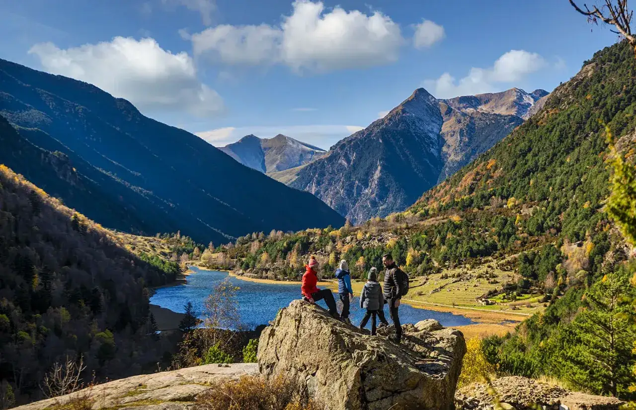 Familia contemplando el impresionante paisaje del Vall de Boí, con montañas, un lago azul y árboles otoñales.