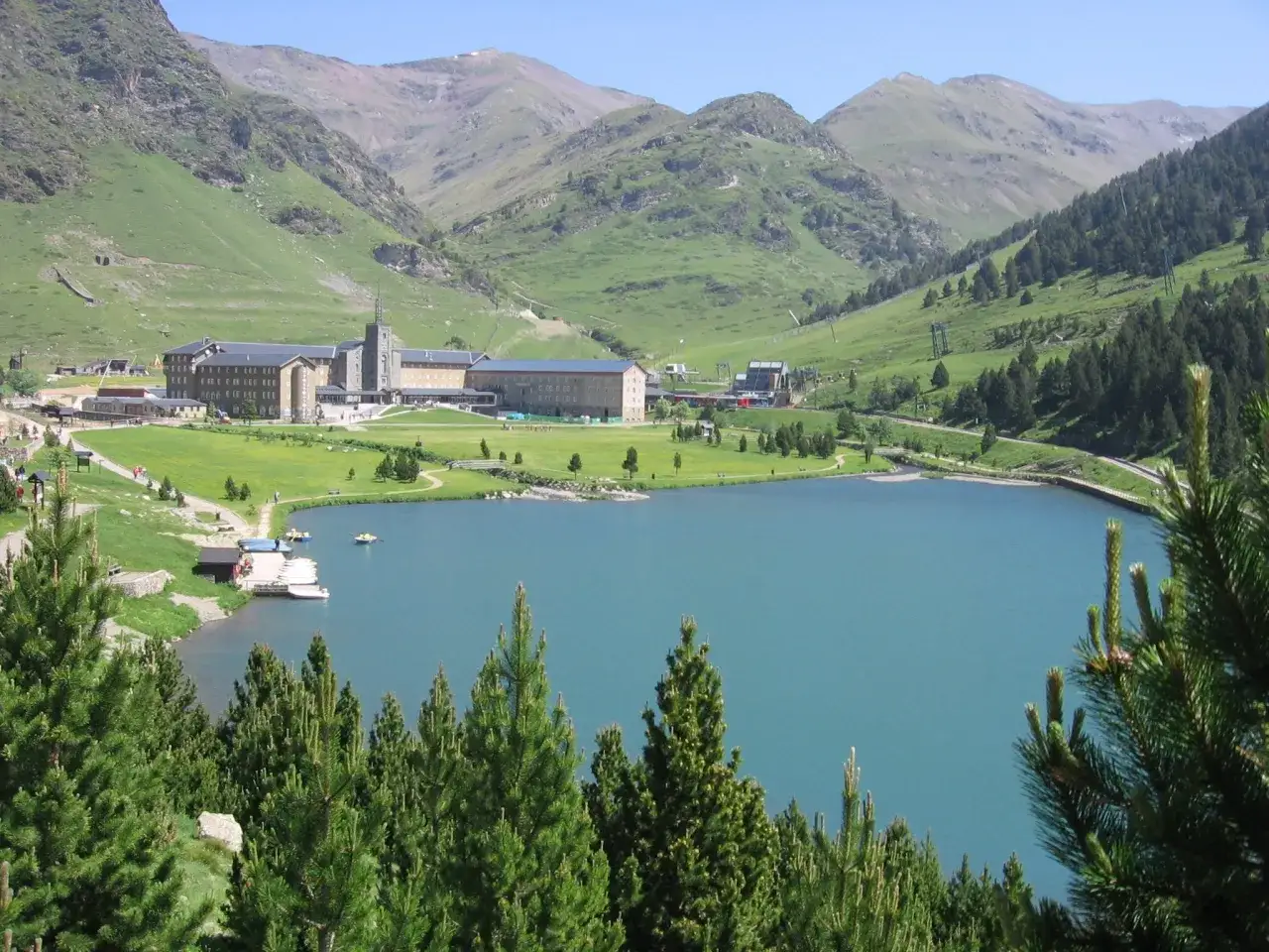 El Valle de Nuria se despliega con un lago turquesa, un santuario imponente y montañas verdes.