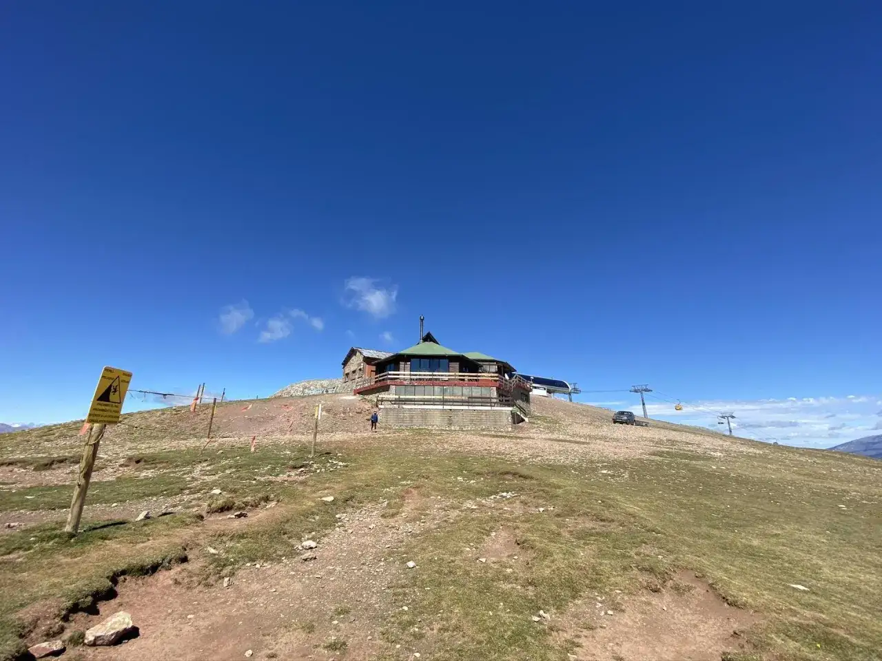 El refugi Cap del Rec se alza en una colina bajo un cielo azul intenso. Un teleférico asciende por la ladera.