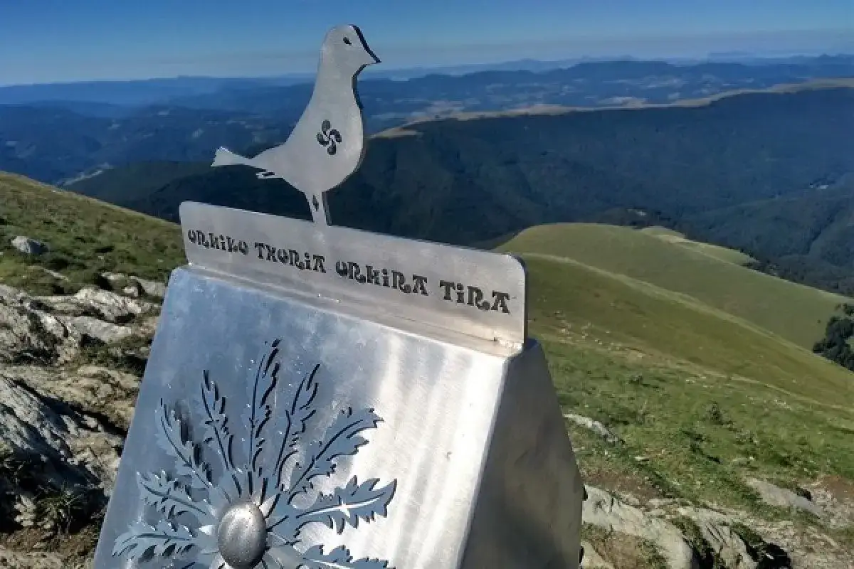 Silueta de pájaro con símbolo vasco en un monumento metálico en la cima de un monte ori, con vistas a un paisaje montañoso verde.