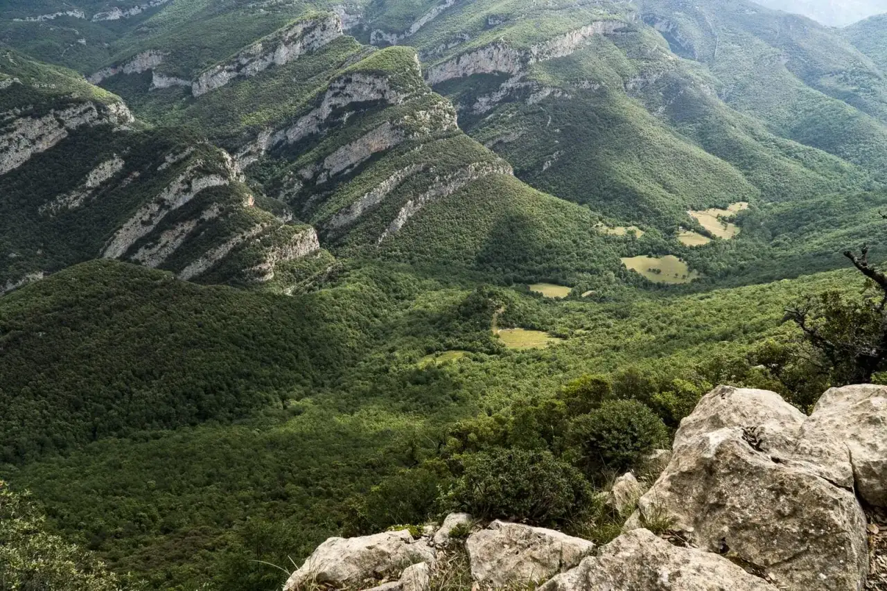 Majestuosas montañas cubiertas de verde en la Alta Garrotxa, con formaciones rocosas y claros soleados.