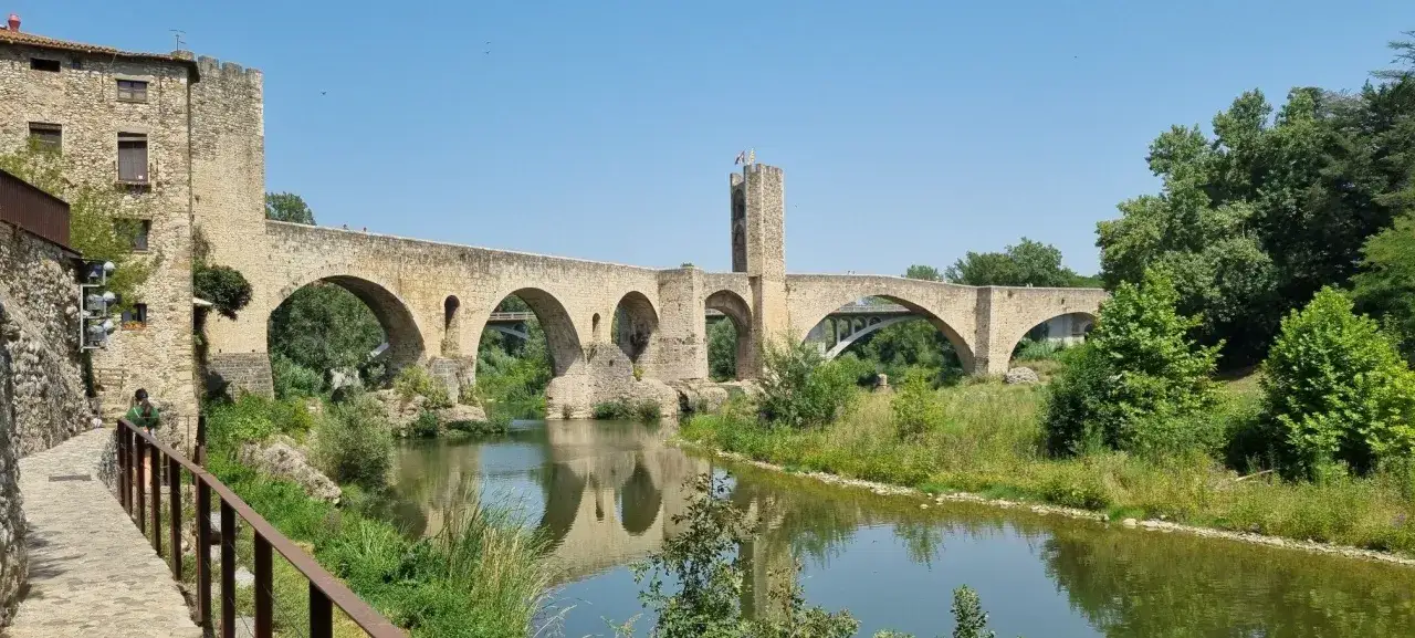 Puente medieval de Besalú, parte de la ruta Besalú, con su torre defensiva y reflejo en el río.