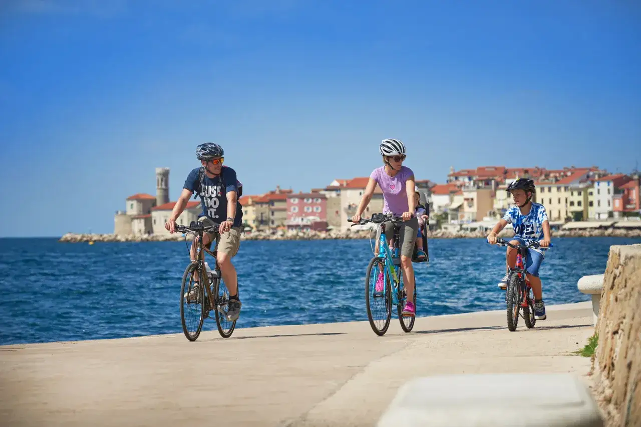 Familia disfruta de un paseo en bicicleta por la costa de Croacia, con edificios históricos al fondo.