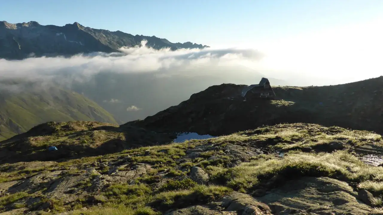 Refugio en la Vall Ferrera al amanecer, con niebla baja entre montañas y tiendas de campaña en la ladera.