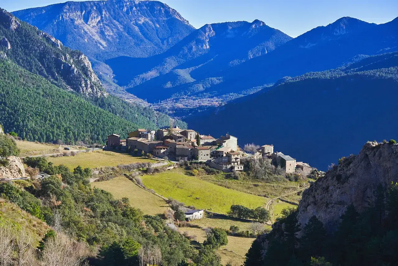 Pueblo de piedra en el Vall de la Vansa, rodeado de montañas azules y verdes prados.