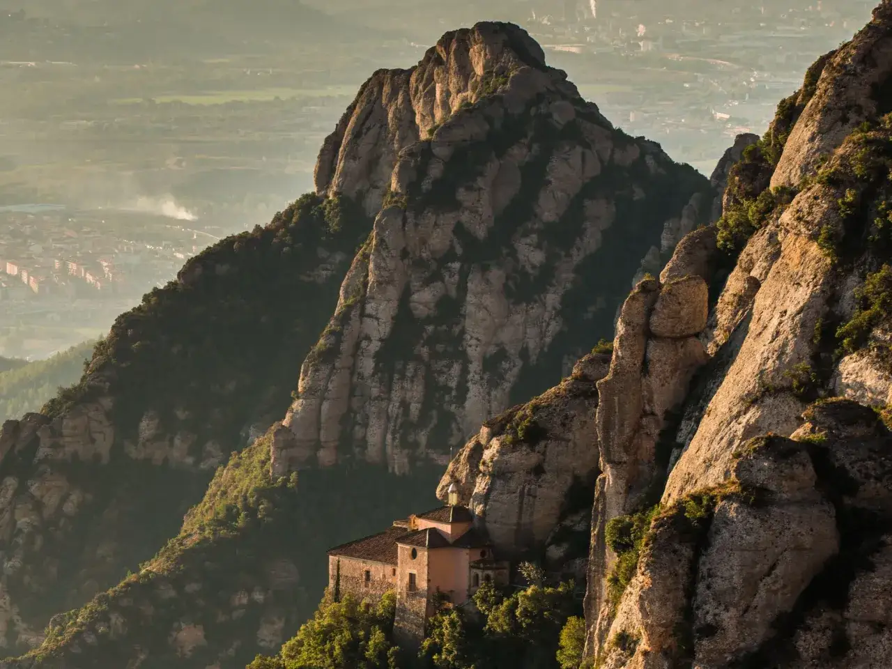 Un monasterio se aferra a las escarpadas laderas del parc natural de la muntanya de Montserrat, con vistas a un valle brumoso.