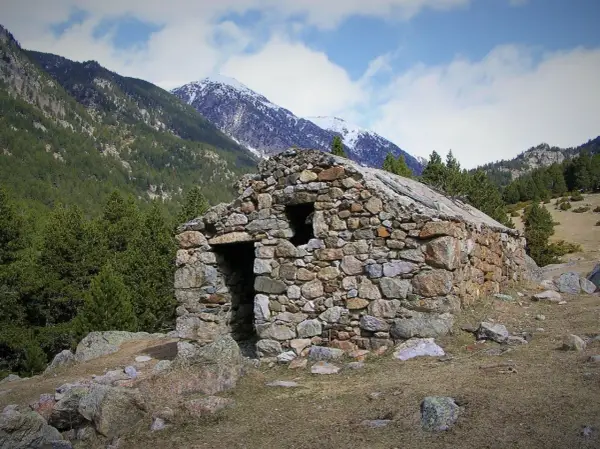 Antigua cabaña de piedra en el Vall de la Llosa, rodeada de pinos y montañas nevadas.