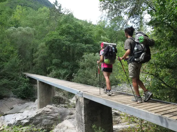 Dos excursionistas con mochilas cruzan un puente de madera en una ruta transpirenaica.