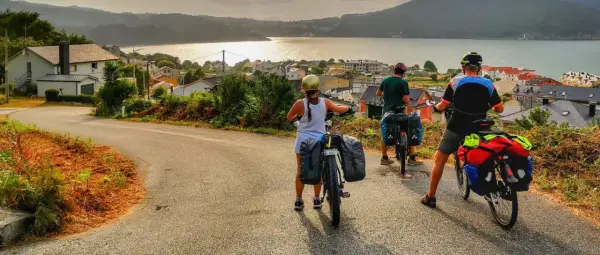 Ciclistas con alforjas exploran **rutas bicicleta** con vistas a un pueblo costero y el mar al atardecer.