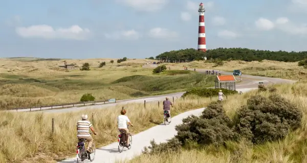 Ciclistas disfrutan de un paseo por la ruta EuroVelo 7, con un faro a rayas rojas y blancas al fondo.
