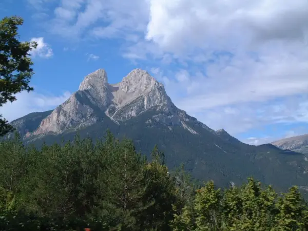 Majestuoso Pedraforca se alza imponente, su altitud desafía las nubes. Bosques verdes cubren sus faldas bajo un cielo azul.